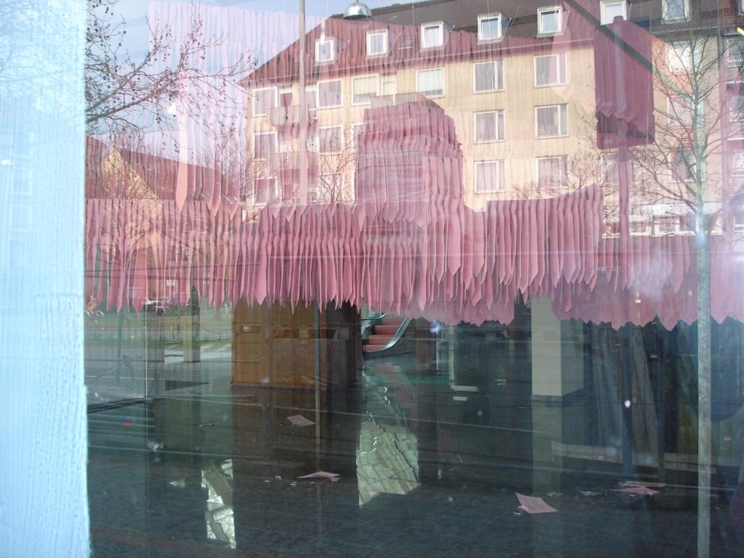 Ausstellung der Krawatten-Installation in einem Schaufenster eines ehemaligen Autohauses in Hannover. Im Schaufenster spiegelt sich auf der Scheibe gleichzeitig ein mehrstöckiges Wohnhaus.