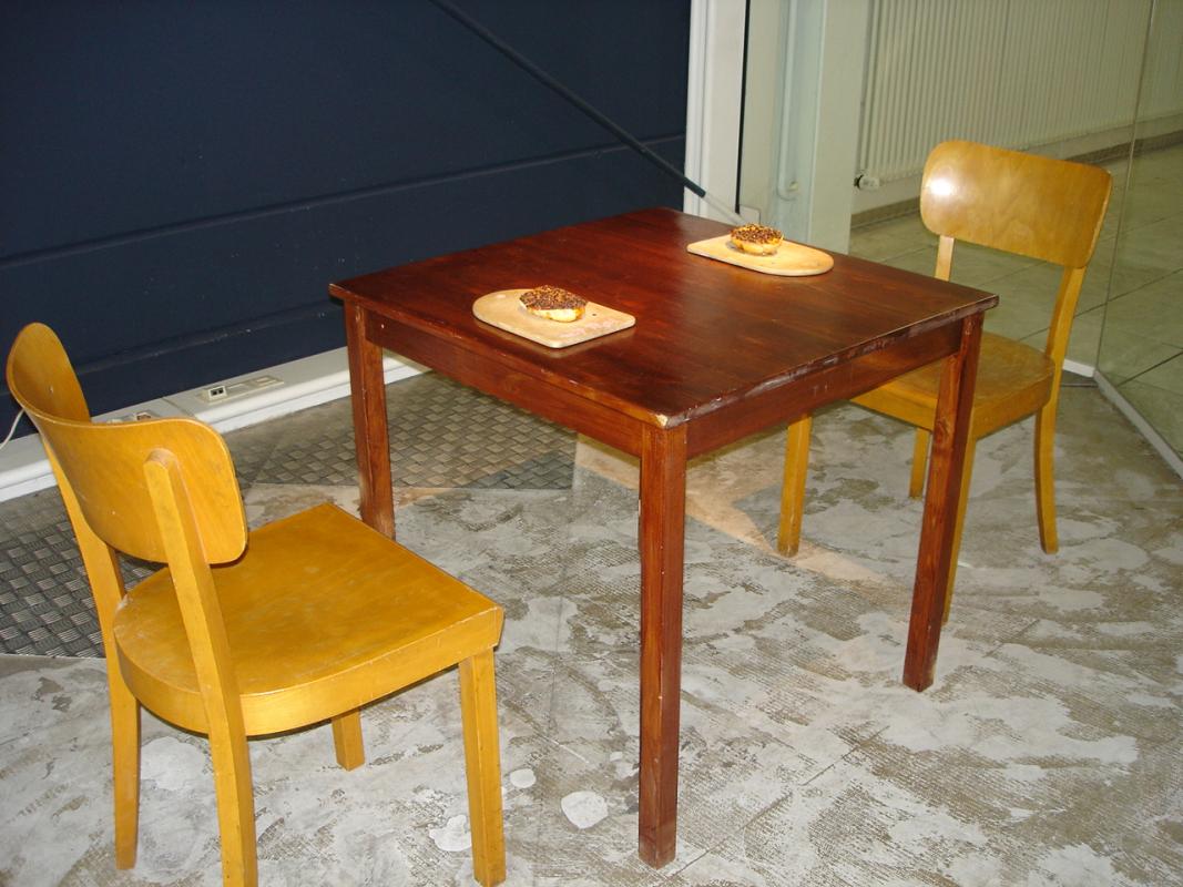Kunstwerk Frühstück mit Papi von Renate Bühn. Holztisch, 2 Stühle, 2 Brötchenhälften auf zwei Frühstücksbrettchen